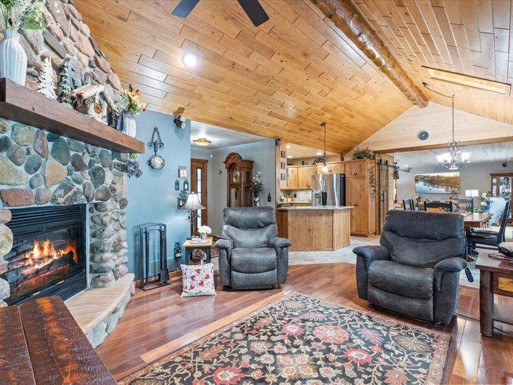 Living room with a stone fireplace, gray recliners, and a vaulted wood ceiling opening to the kitchen.