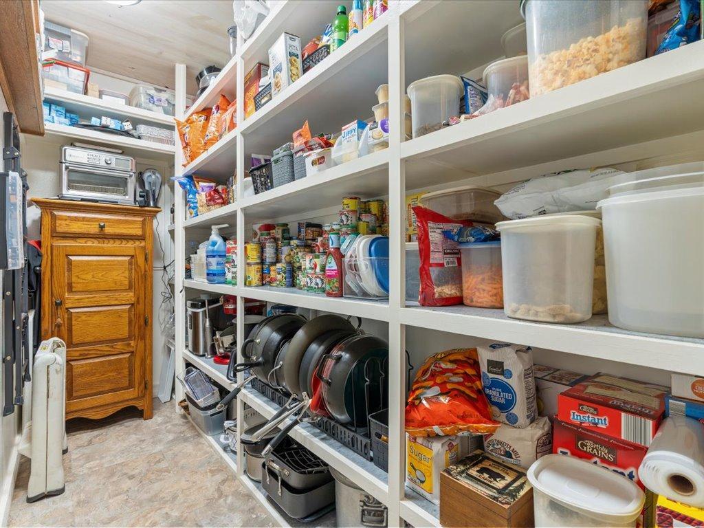 Walk-in pantry with shelves of groceries, clear food containers, and cookware.