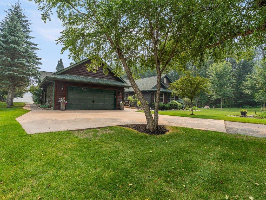 Dark wood house with a two-car garage, wide driveway, and mature trees.