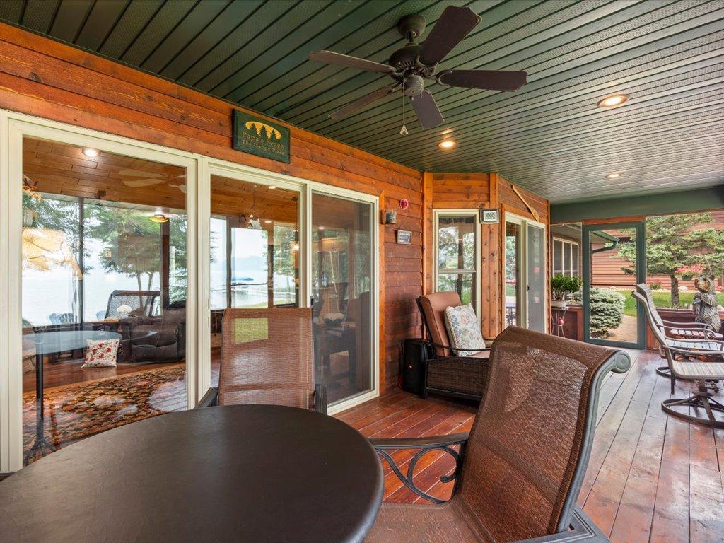 Covered lakeside deck with wicker seating, wood walls, and a view of the water through glass doors.