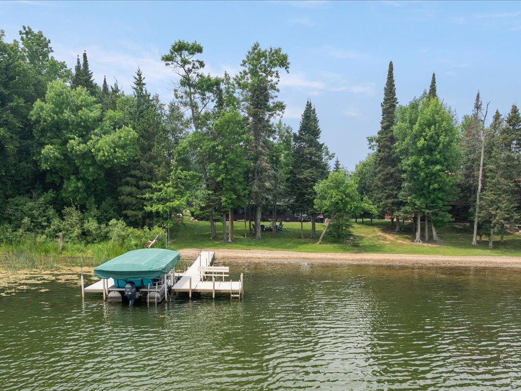 Lakefront shoreline with a covered boat lift, dock, and wooded lawn.