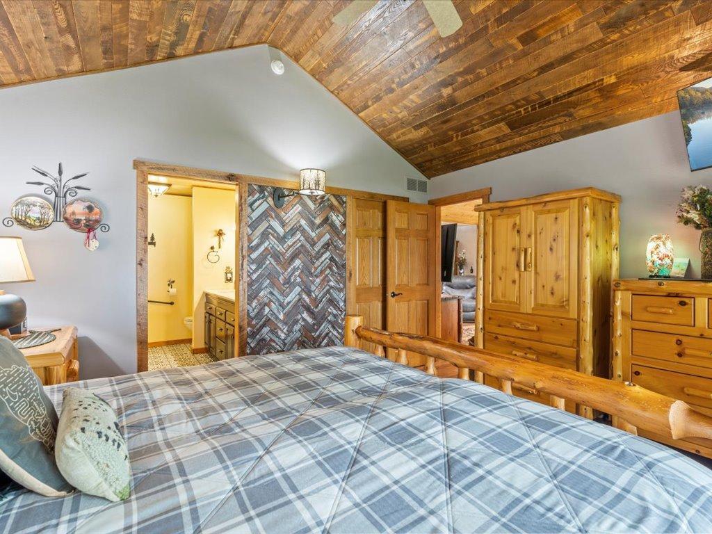 Bedroom with a plaid bed, vaulted wood ceiling, and rustic log furnishings.