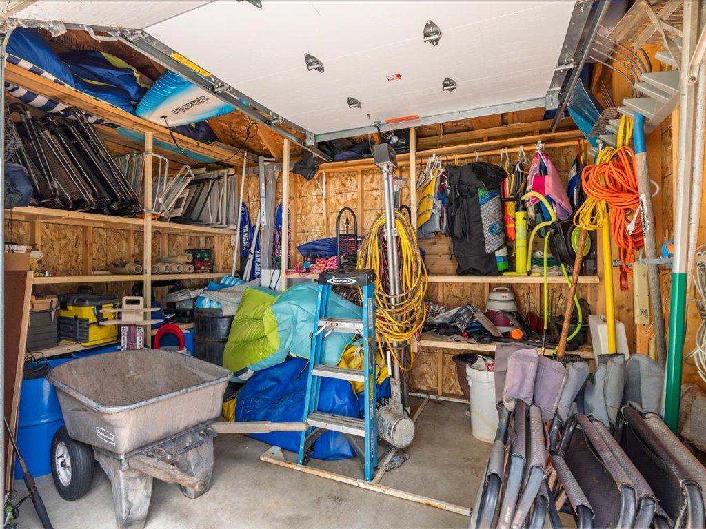 Garage packed with outdoor gear, including overhead kayaks, a wheelbarrow, ladders, and coiled hoses.