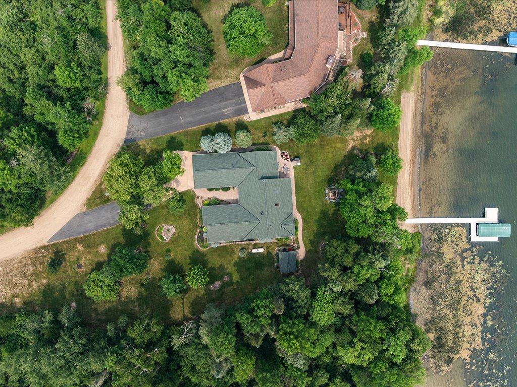 Aerial view of a lakeside house surrounded by trees, with a dock on the shoreline.