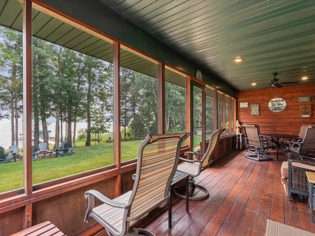 Furnished lakeside porch with screened windows overlooking a green lawn and water.