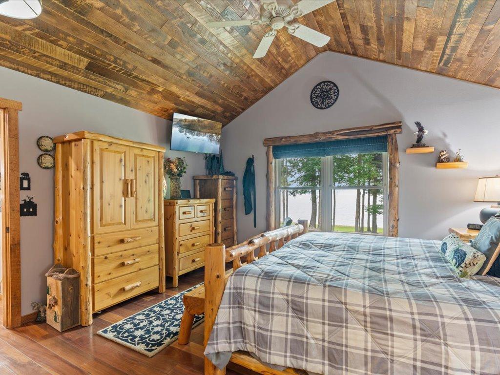 Bedroom with a log bed, plaid bedding, patchwork wood ceiling, and a lake view through the window.