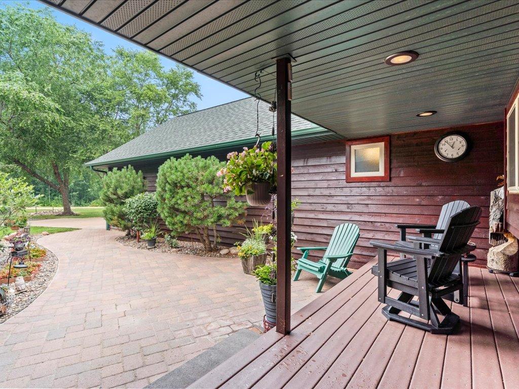 Covered deck with Adirondack chairs beside a landscaped paver patio.