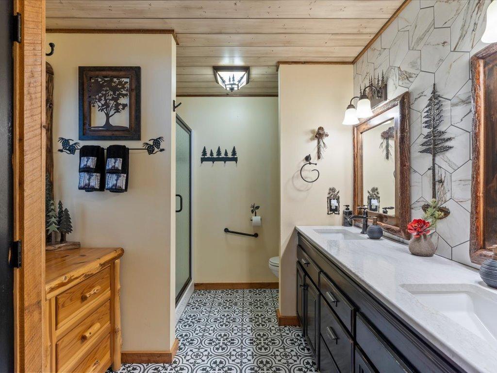 Bathroom with a dark wood vanity, marble-look wall tile, patterned floor, and glass-enclosed shower.