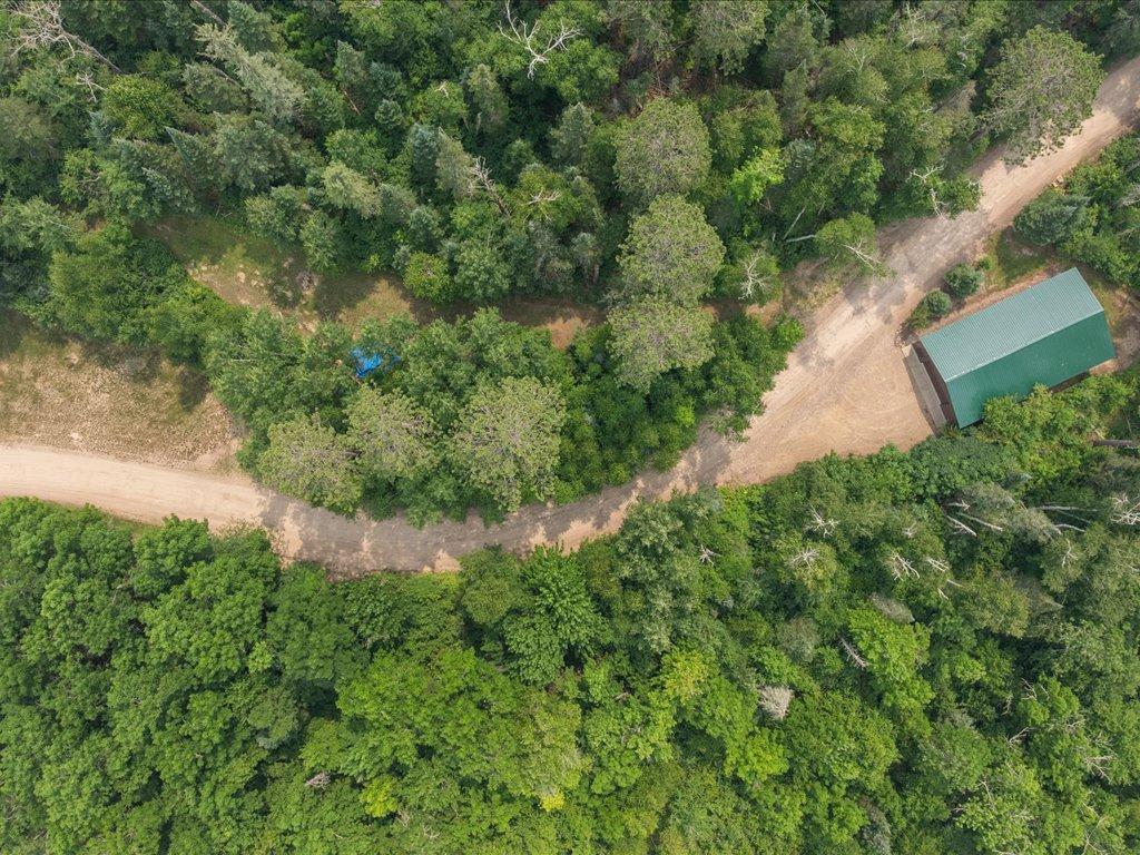 Aerial view of a wooded property with a dirt road and green-roofed outbuilding.