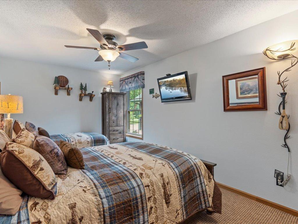Bedroom with plaid bedding, a ceiling fan, and rustic wall decor.