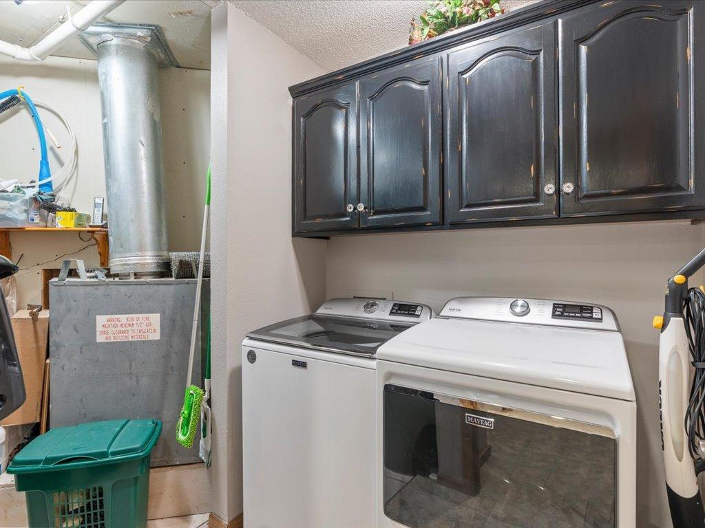 Laundry room with a washer and dryer beneath dark cabinets beside a utility area.