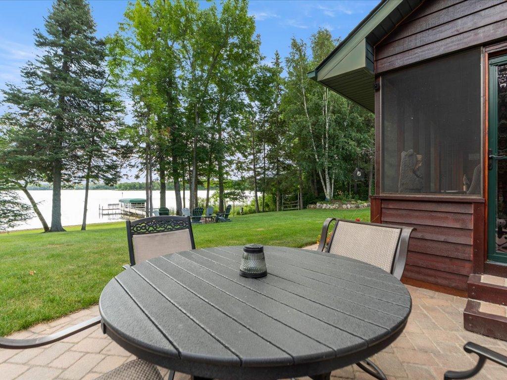 Patio dining table overlooking a grassy lawn, wooded lakefront, and dock.