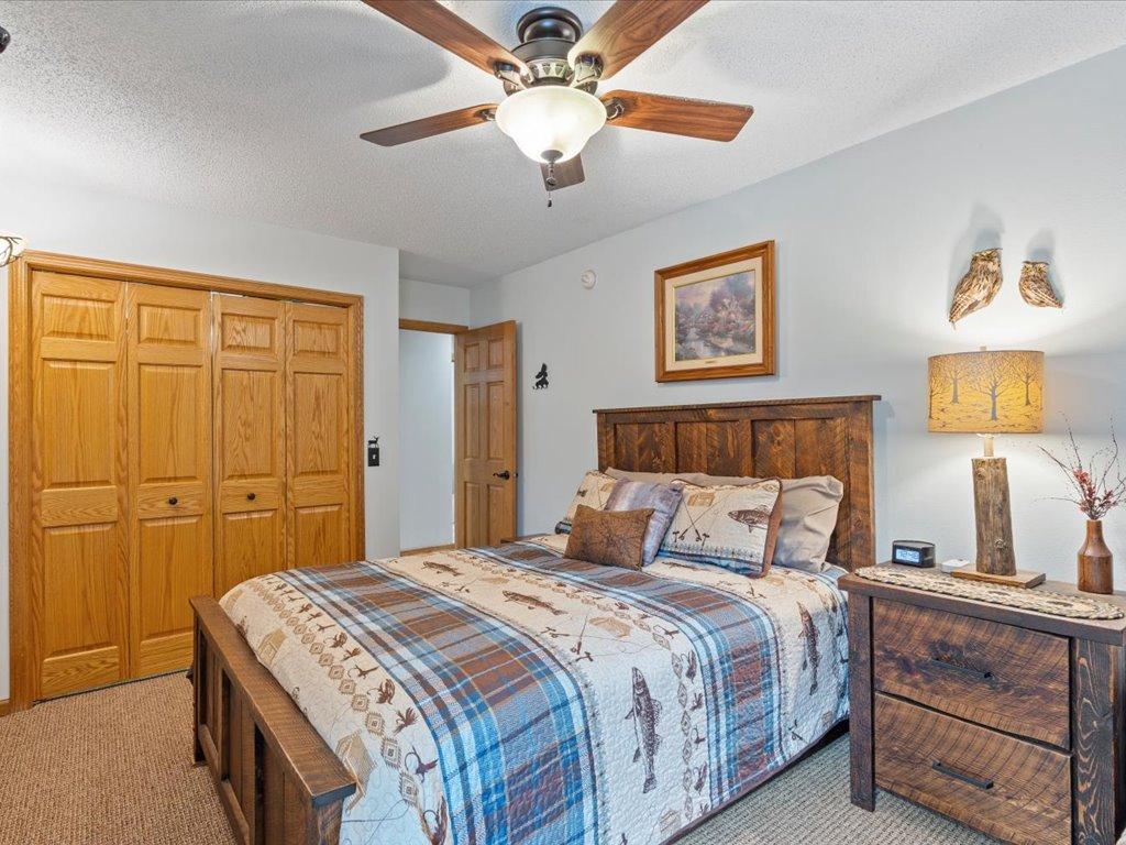 Bedroom with a dark wood bed, blue plaid quilt, oak closets, and ceiling fan.