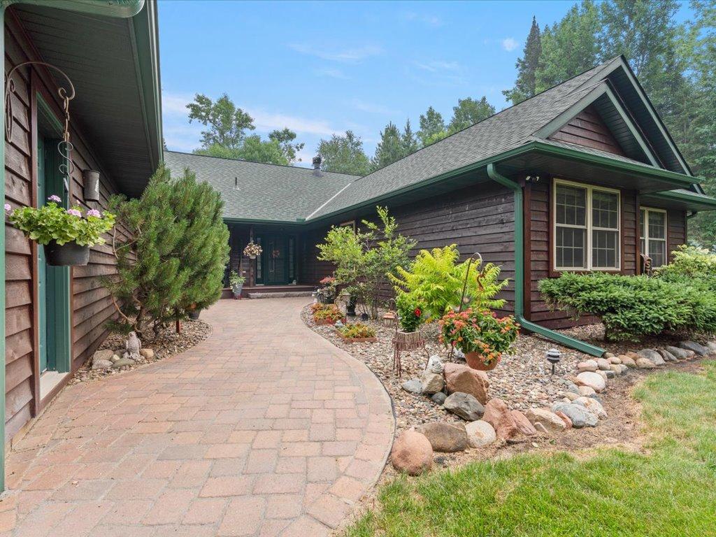 Dark wood-sided home with green trim, curved brick walkway, and landscaped rock gardens.