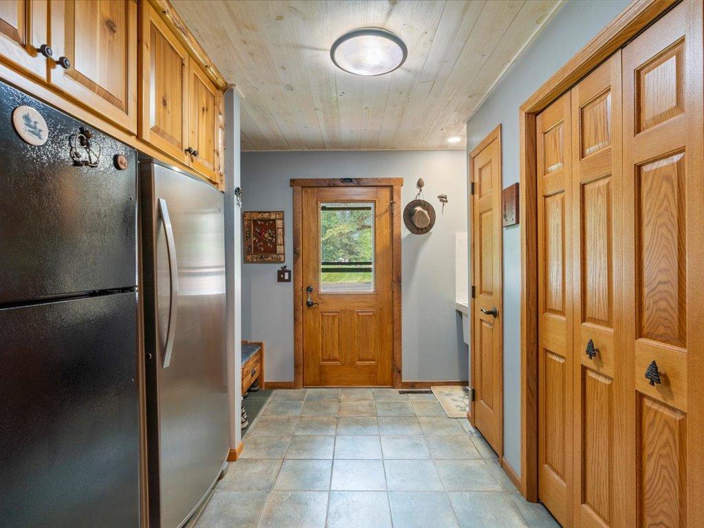 Entryway with tiled floor, wood cabinetry, refrigerator, and a wood-framed door with a window.