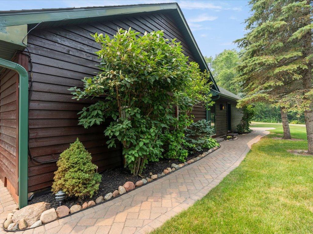 Dark wood-sided home with green trim, leafy shrubs, and a curved brick walkway.