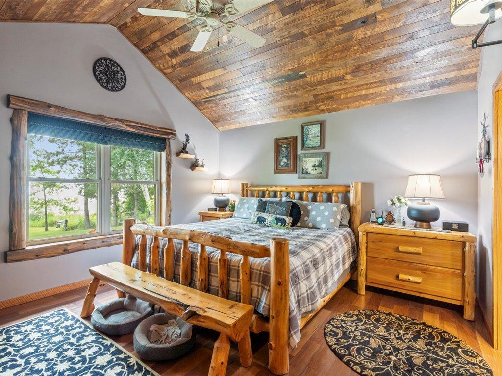 Bedroom with a log bed beneath a vaulted wood-plank ceiling and a large yard-facing window.