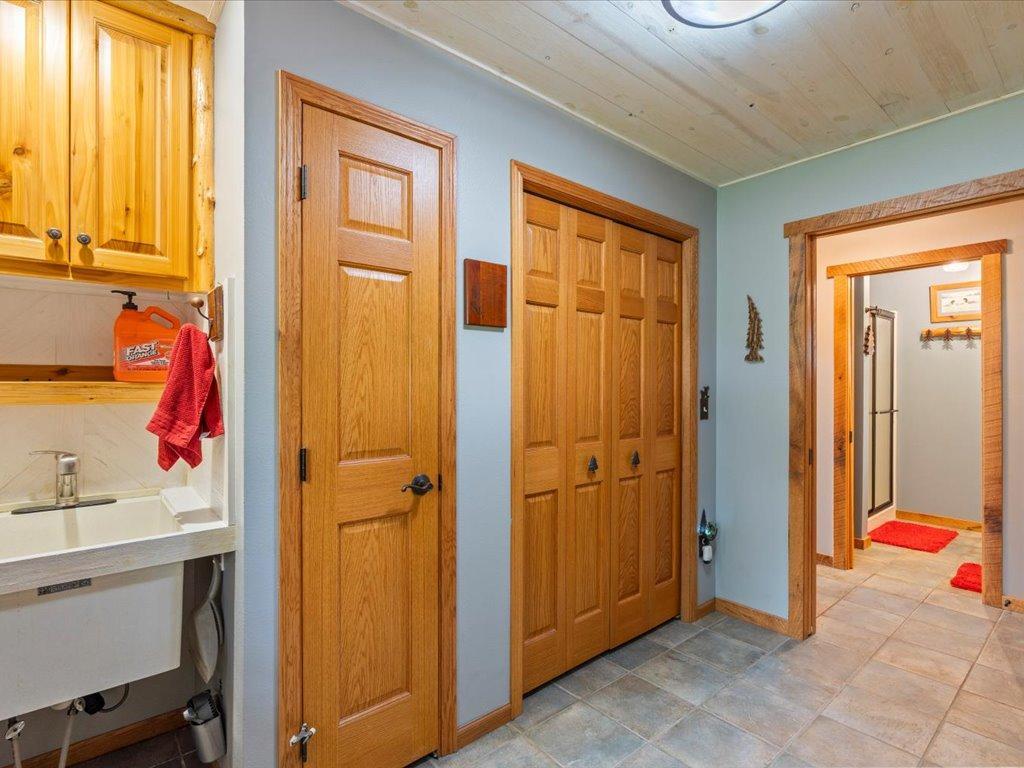 Utility room with a deep sink, honey-colored wood cabinets, double closet doors, and tiled flooring.