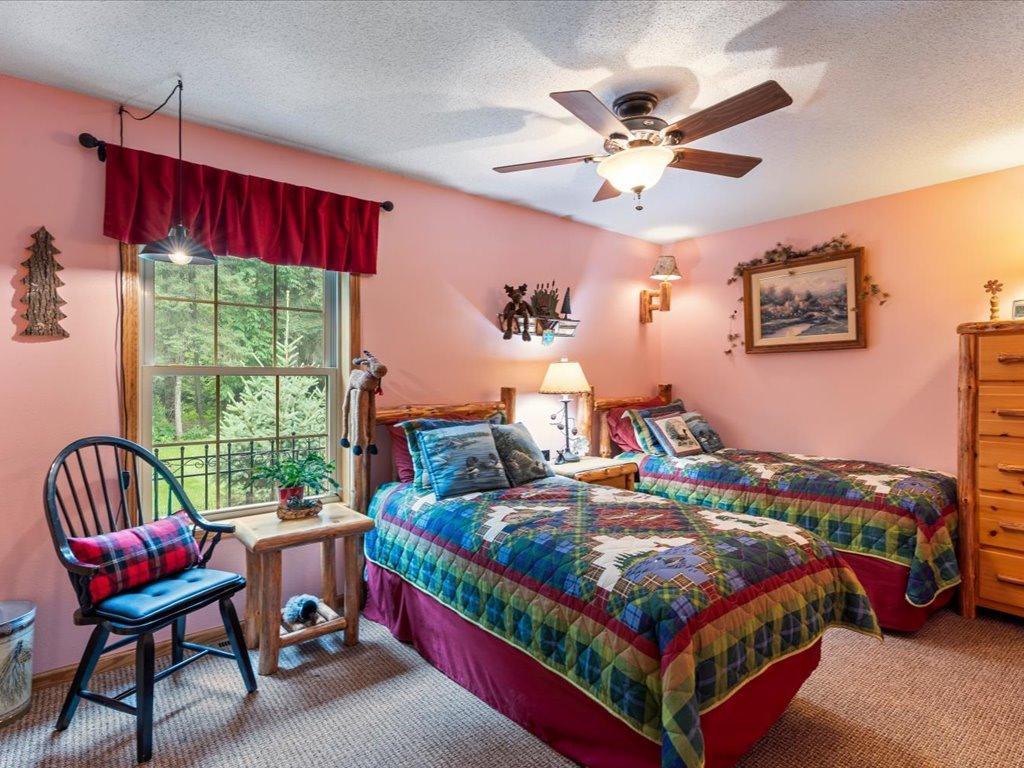 Bedroom with two colorful patchwork-covered beds beside a large window overlooking trees.
