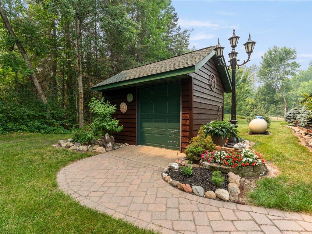 Detached dark wood garage with a green door beside a curved paver driveway and flower beds.