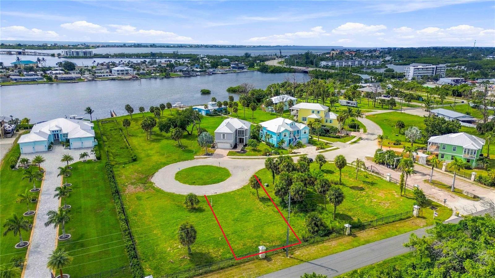 Vacant lot outlined in red, with palm trees, nearby homes, and water in the distance.