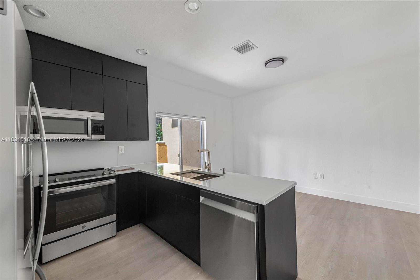 Modern kitchen with dark cabinets, stainless appliances, and a white island with sink.