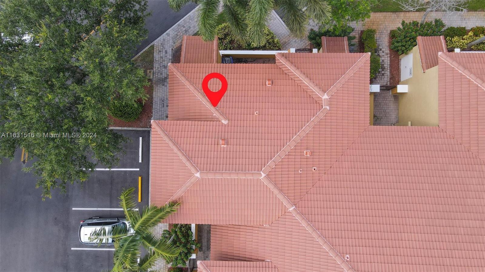 Aerial view of terracotta-roofed homes with a red location marker on one roof.