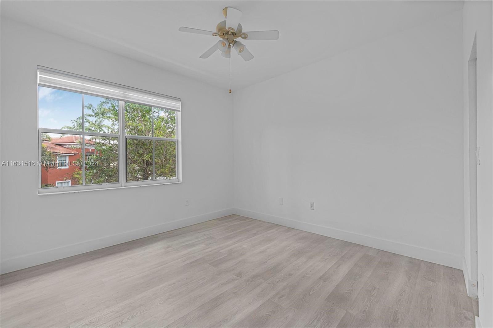 Empty bedroom with pale wood-look flooring, a ceiling fan, and a large window.