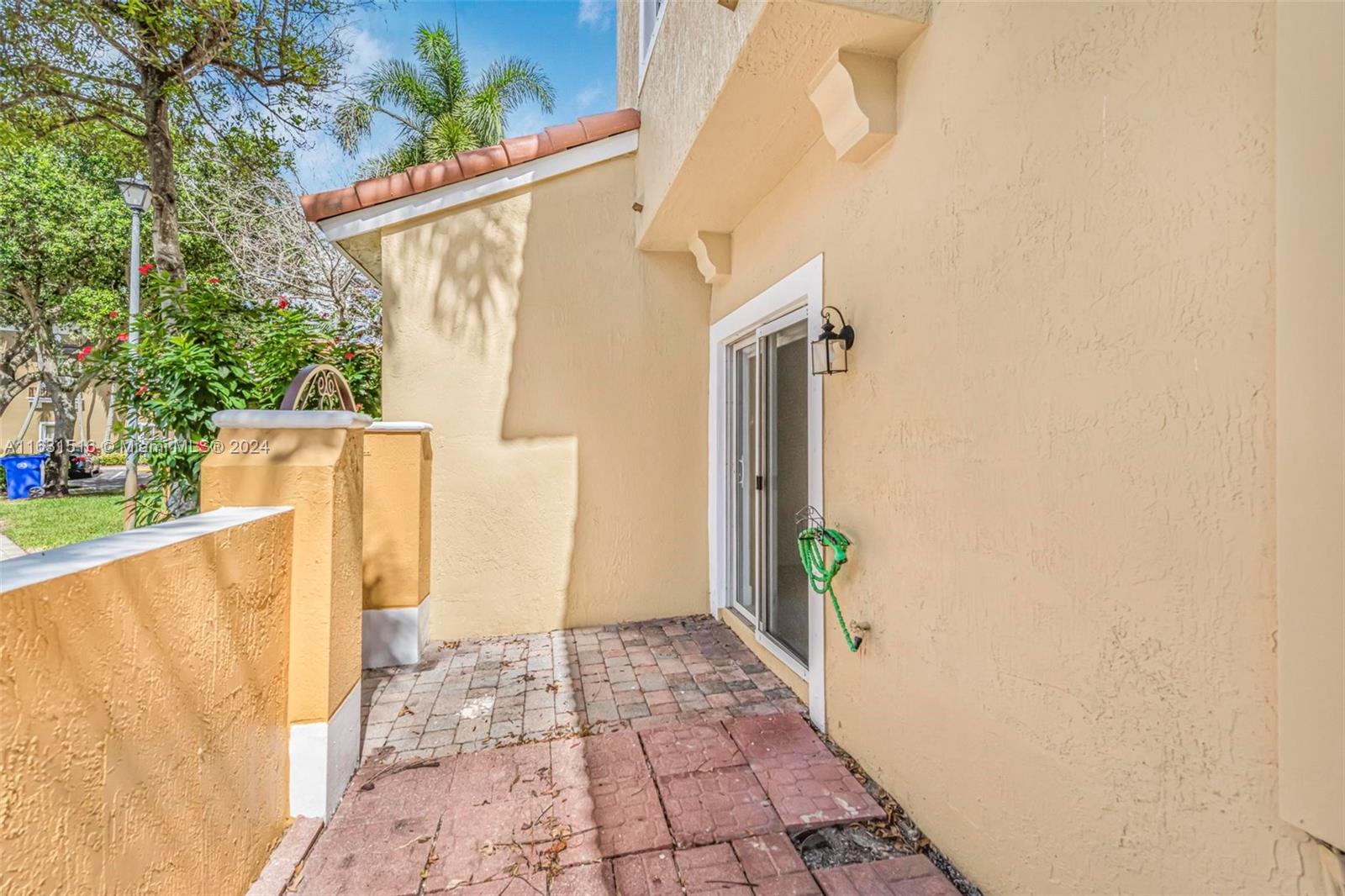 Paved patio beside a beige stucco home, with a sliding glass door and low courtyard walls.