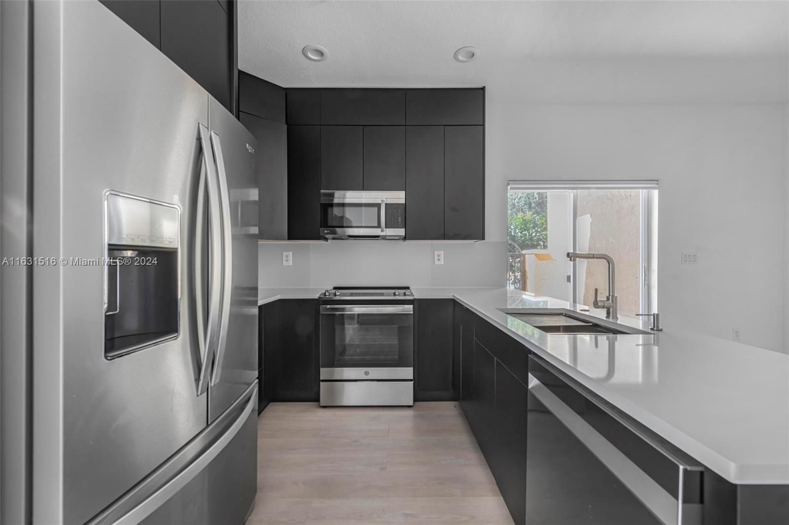 Modern kitchen with dark cabinetry, stainless steel appliances, and a long white peninsula with sink.