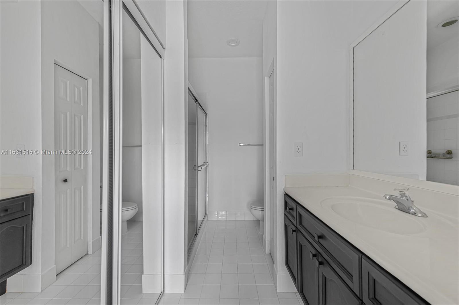 Bathroom with dark cabinetry, white countertop, large mirror, and glass-enclosed shower.