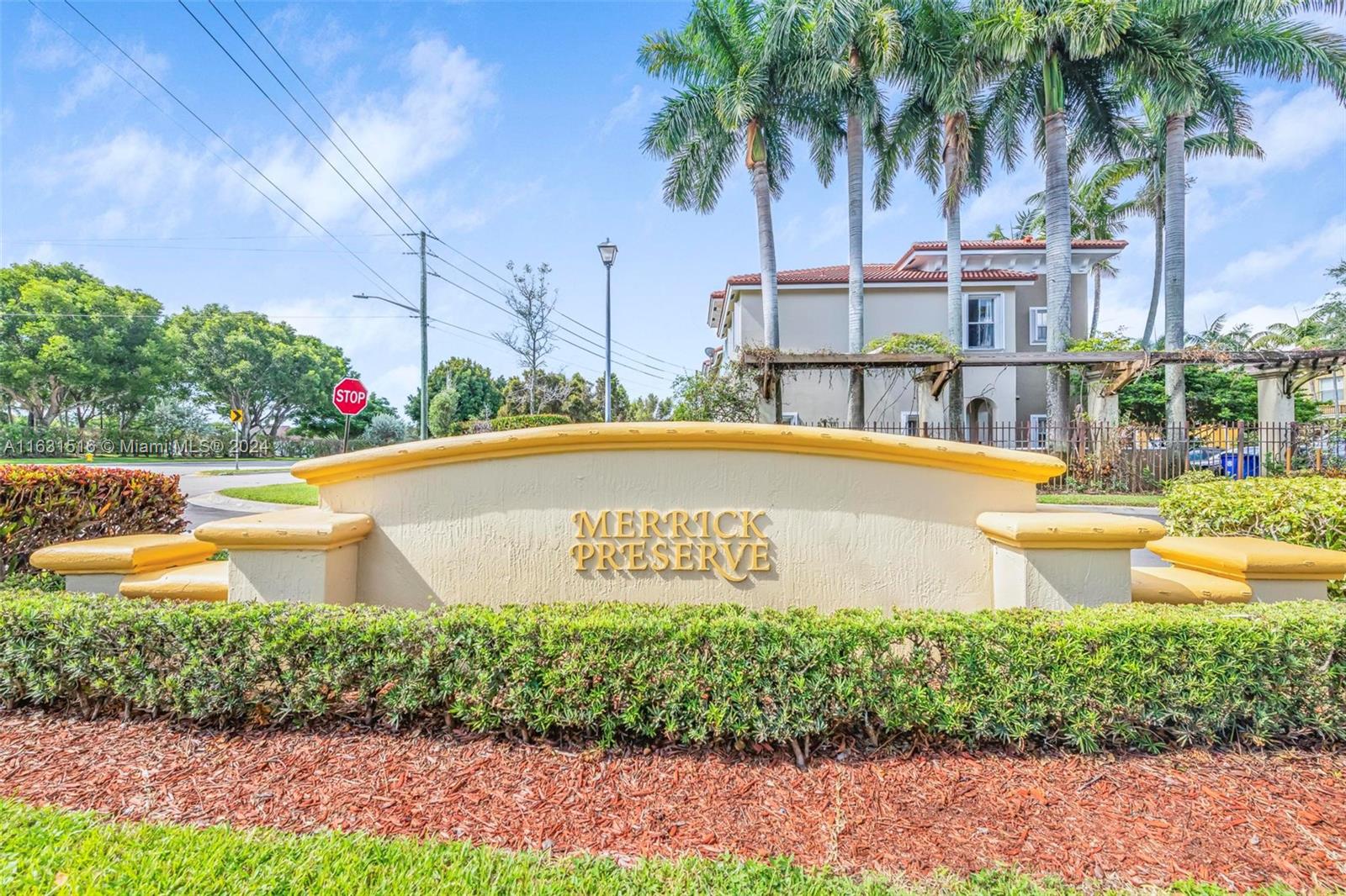 Merrick Preserve entrance sign with tall palm trees and a residential building behind it.