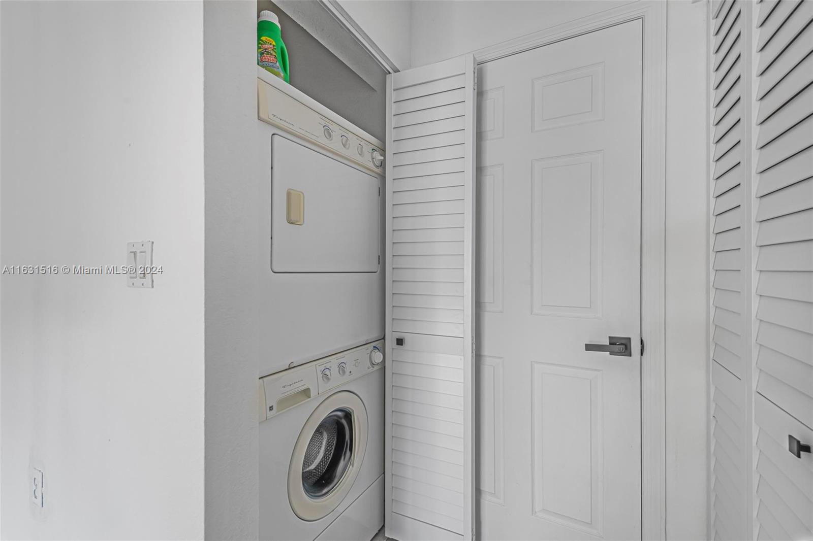 Stacked washer and dryer in a laundry closet with white louvered doors.