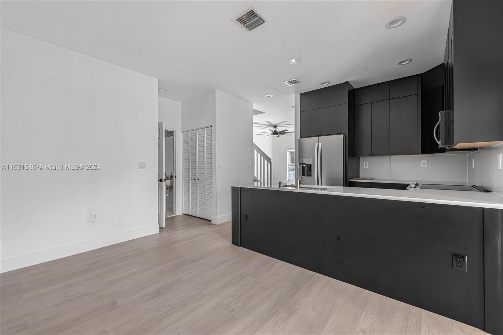 Modern kitchen with dark cabinets, a large white-countertop peninsula, and stainless steel refrigerator.