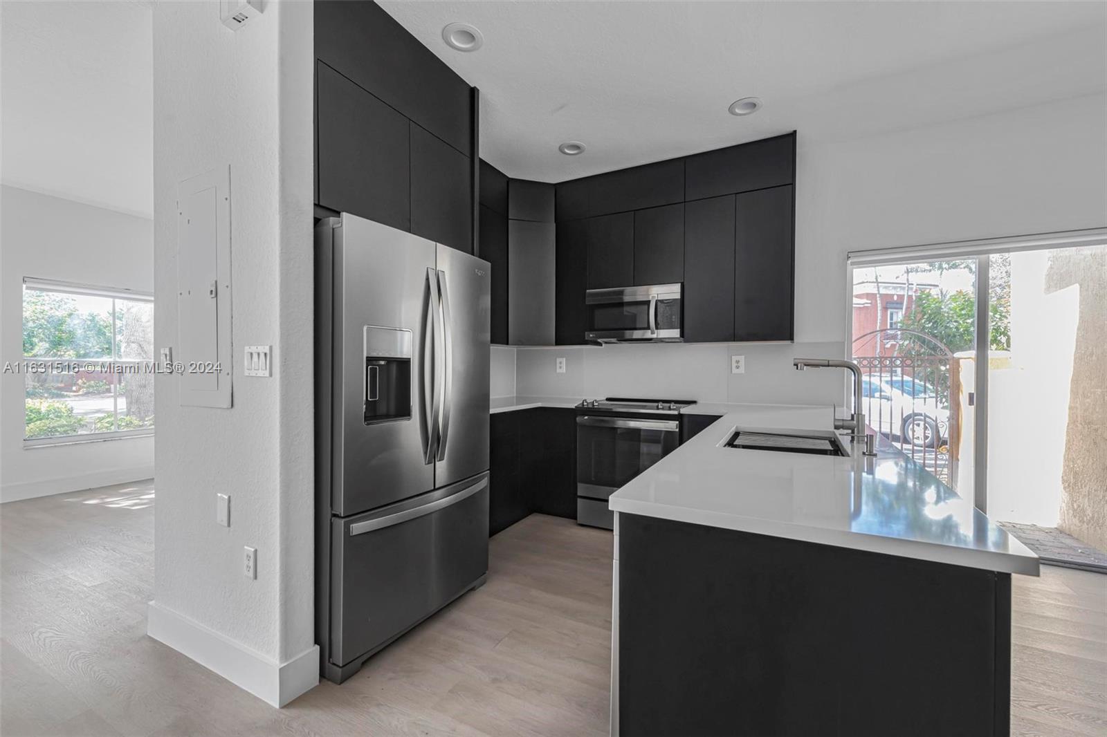Modern kitchen with dark cabinets, stainless appliances, and a white island beside sliding glass patio doors.