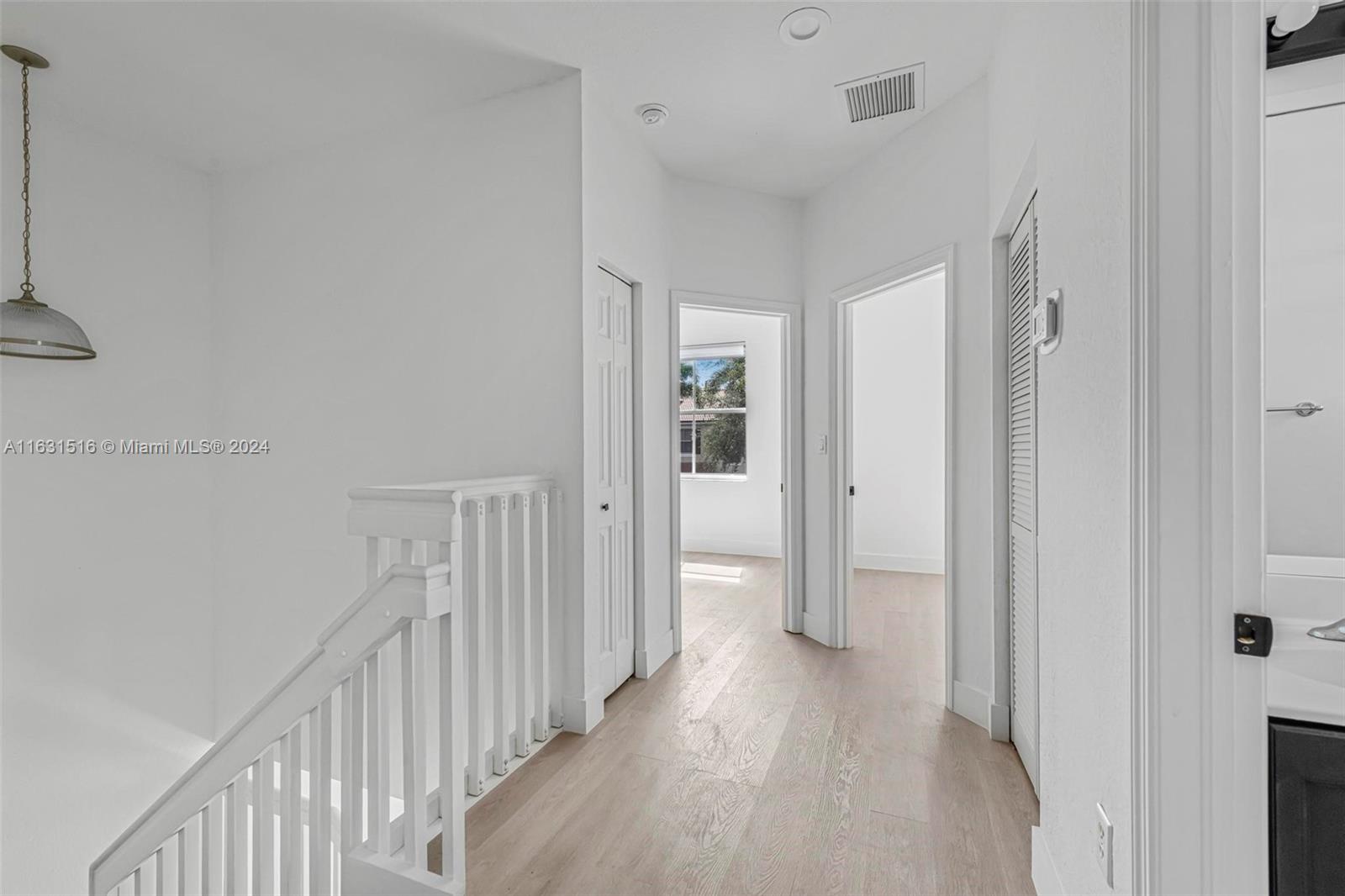 Unfurnished upstairs hallway with pale wood-look flooring, white stair railing, and a window at the end.