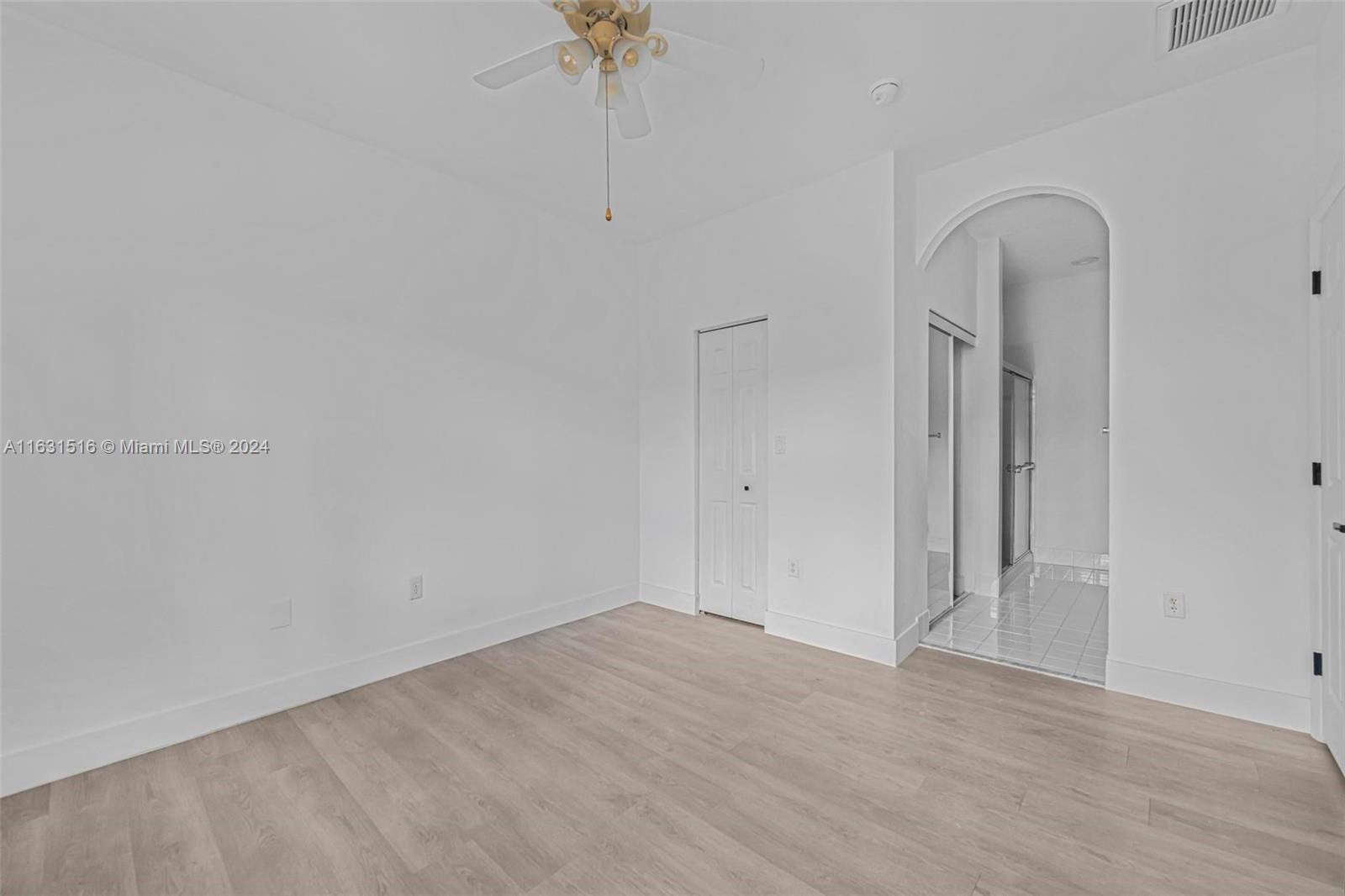 Vacant bedroom with light wood-look flooring and an arched opening to a tiled bathroom.