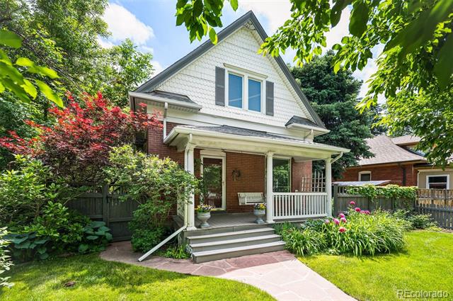 White-and-brick house with a covered front porch, white railings, and lush gardens.