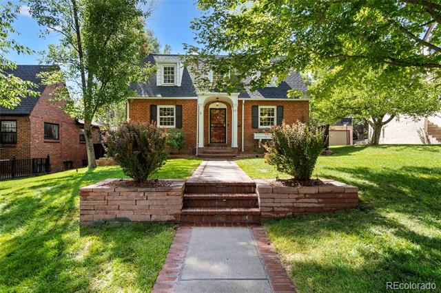 Two-story brick home with an arched entry, raised brick terrace, and tree-shaded lawn.