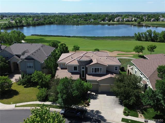 Aerial view of a home beside a lake, with neighboring houses and green lawns.