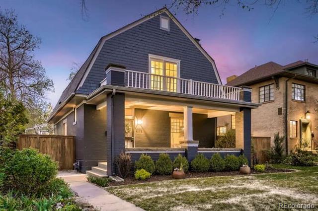 Dark blue two-story home with a steep roof, covered porch, and illuminated windows at dusk.