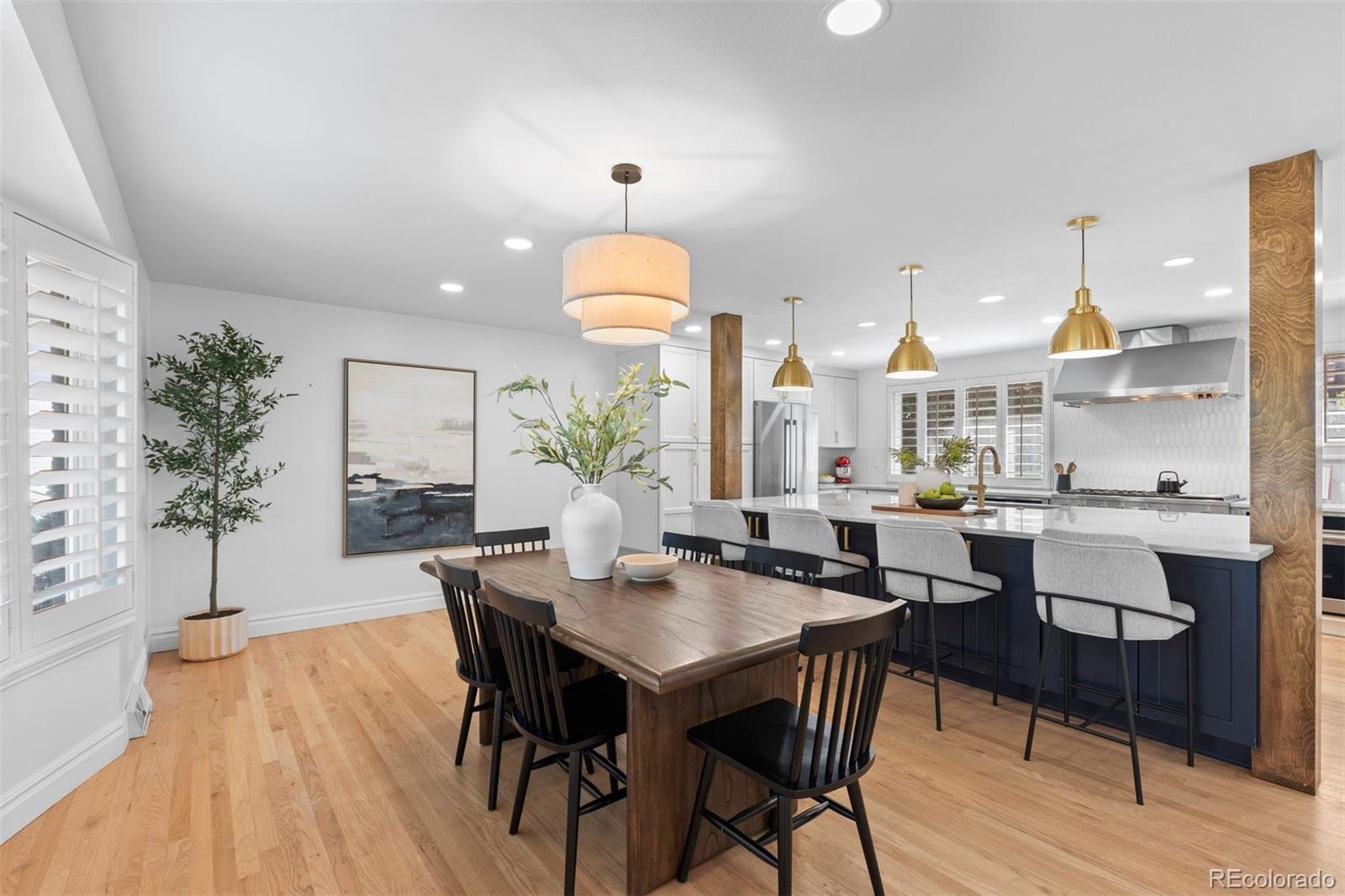 Dining area with a wood table beside a dark island and bright white kitchen.