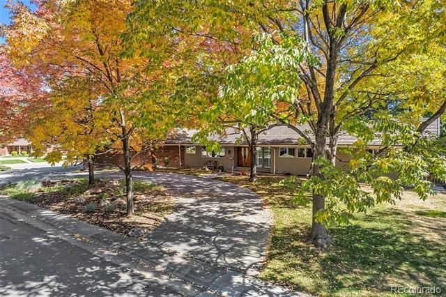 Single-story house with a covered porch behind colorful autumn trees and a paved driveway.