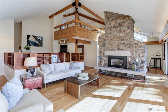 Living room with a stone fireplace, vaulted timber ceiling, and loft railing.
