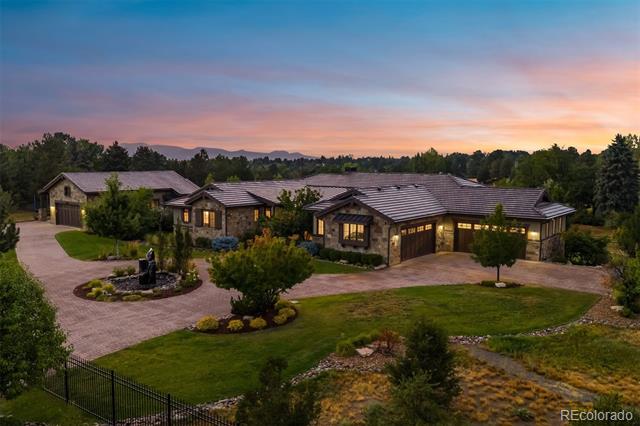 Stone ranch home with a curved driveway and landscaped lawn at sunset.