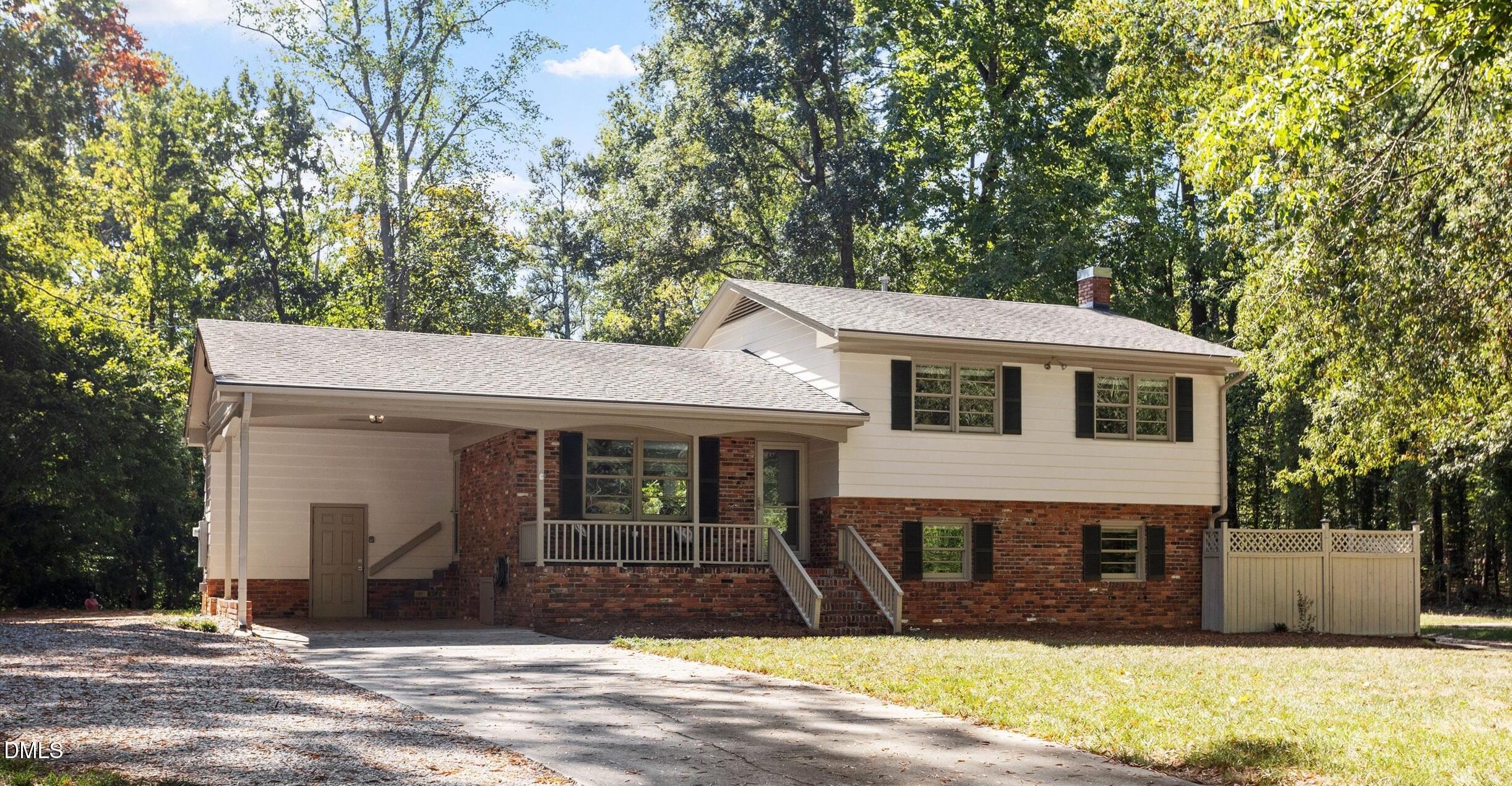 Split-level home with cream siding, red brick, a covered carport, and mature trees.
