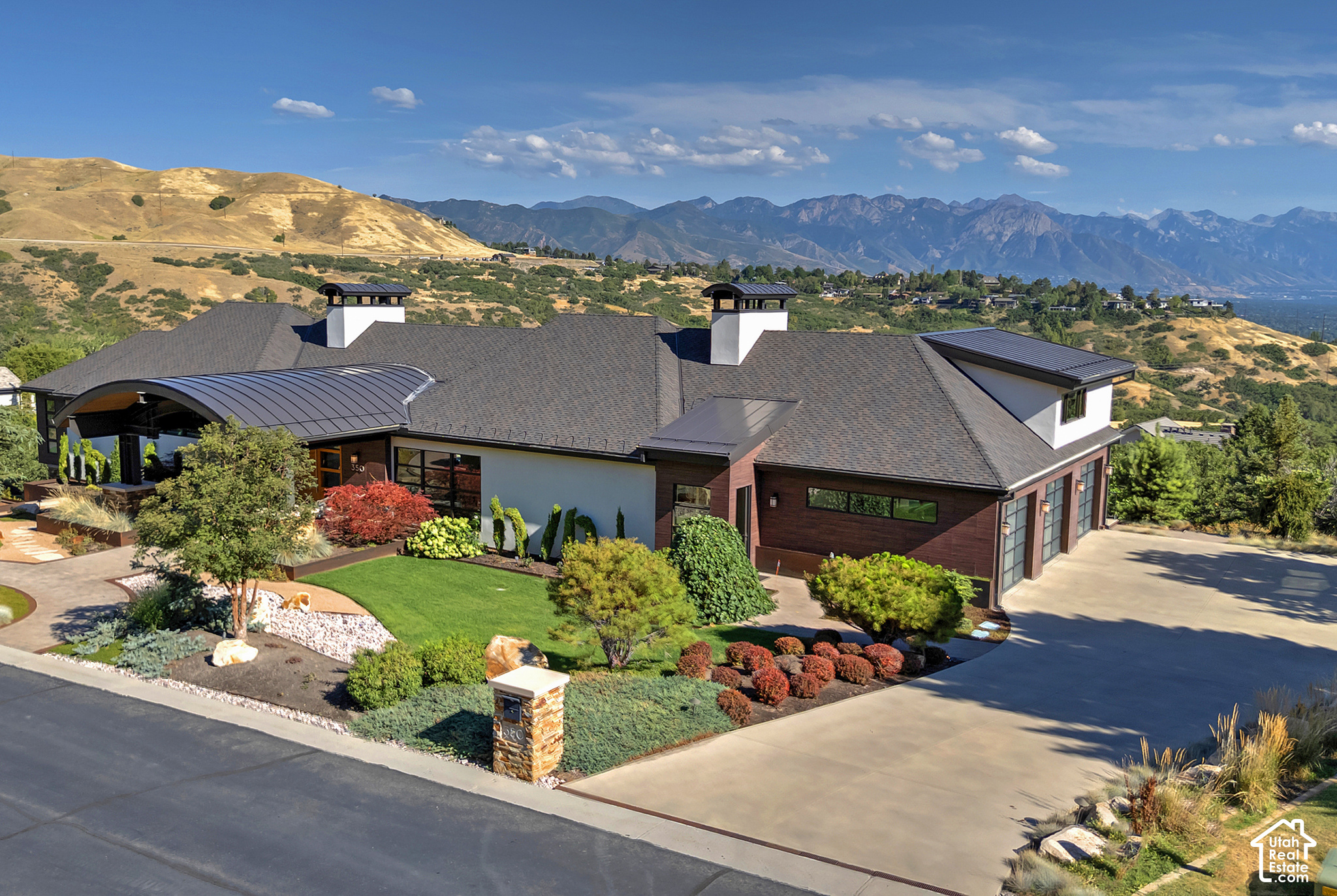 Modern home with landscaped grounds and a broad driveway, backed by mountain views.