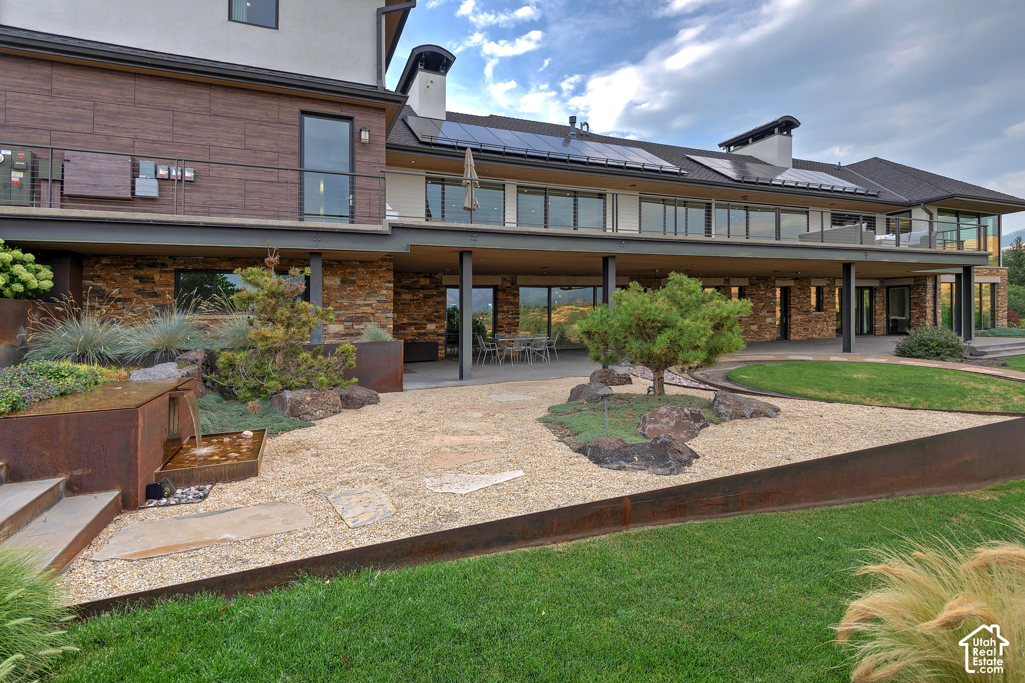 Modern home with solar panels, covered patio, and landscaped gravel courtyard with a water feature.