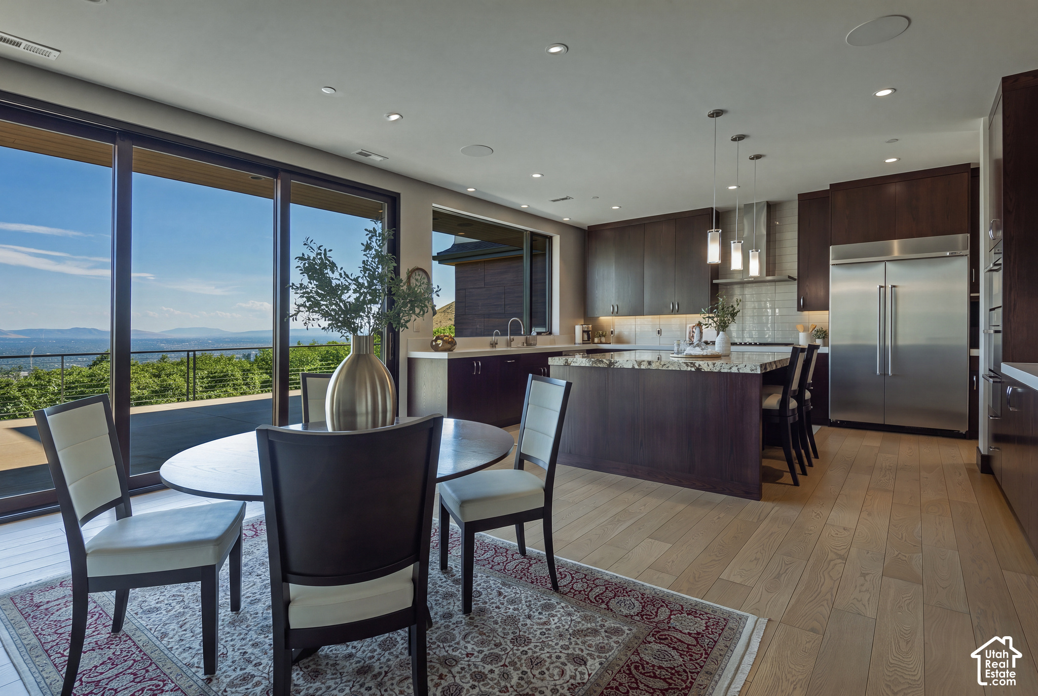 Modern kitchen and dining area with a large island and expansive windows overlooking water and mountains.