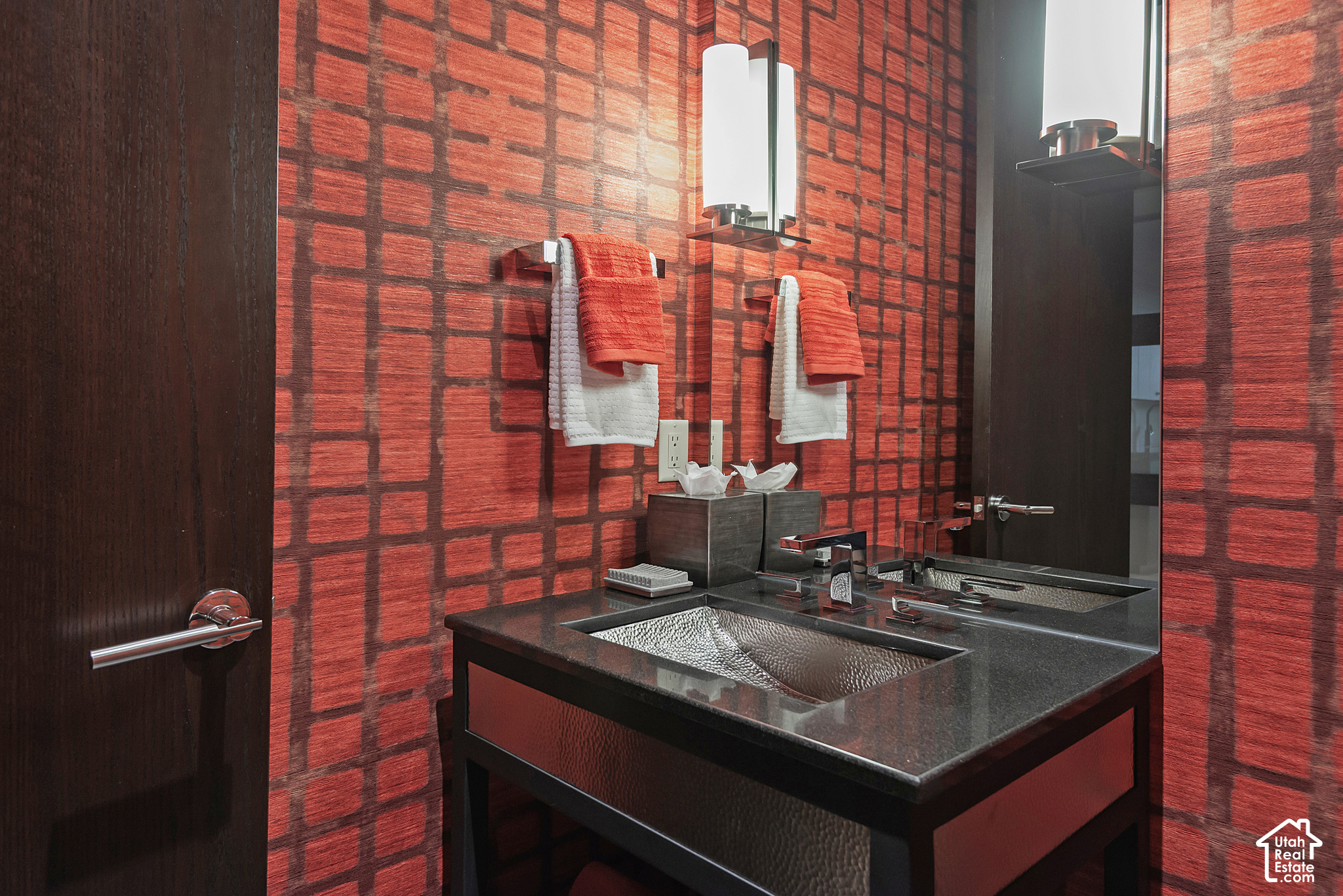 Bathroom vanity with a hammered-metal vessel sink, mirrored wall, and bold red patterned wallpaper.